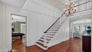 Un interior espacioso con una imponente escalera, pisos de madera y un candelabro.