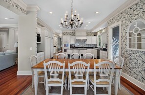A dining area with a wooden table and white chairs, surrounded by white cabinetry and a patterned wallpaper.