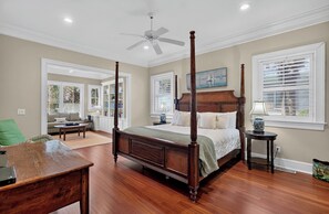 A four-poster bed with a wooden headboard, a ceiling fan, and a view of the outdoors through a window with blinds.