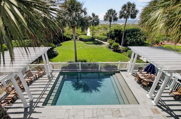 A pool area with a clear view of the ocean, surrounded by palm trees and a well-maintained lawn.