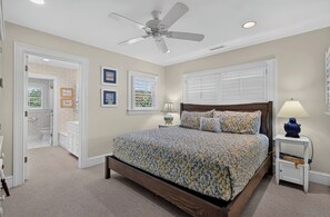 Une chambre à coucher avec un lit, un ventilateur de plafond, une fenêtre avec des stores et une table de chevet avec une lampe.