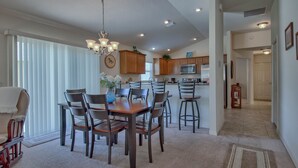 A spacious dining area with a wooden table and chairs, a chandelier, and a view of the kitchen in the background.