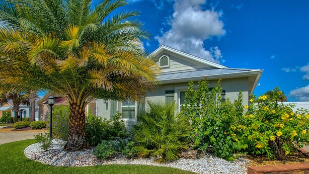 A two-story house with a well-maintained garden, including a palm tree and various flowering plants.