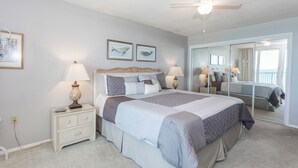A bedroom with a large bed, two bedside tables with lamps, a dresser, and a mirror. - E904 3 Gulf-front pools, Stunning Beach View, Tennis Courts (Panama City Beach)