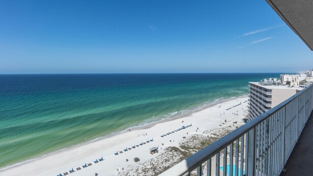 A beach view from a balcony with a clear sky, a sandy beach, and a hotel building with a pool. - E1706 Gulf Front View, 3 Pools, Gated Condo (Panama City)