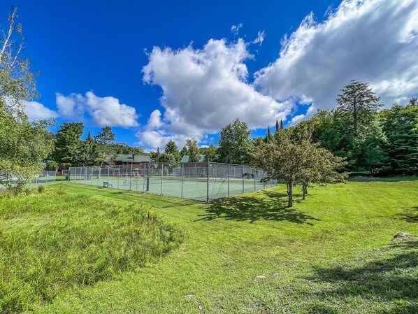 Ein Tennisplatz mit Zaun, Bäumen und blauem Himmel.