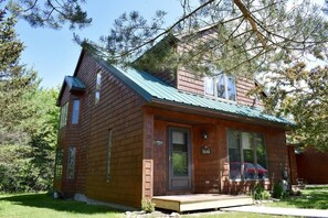 A two-story wooden cabin with a green metal roof, a front porch, and a mailbox. - Townhome J1 - Vacation Rental on 4th Lake (Inlet)