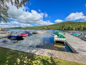 A marina with boats docked, a wooden dock, and a lake with a forested hill in the background. - Townhome J1 - Vacation Rental on 4th Lake (Inlet)
