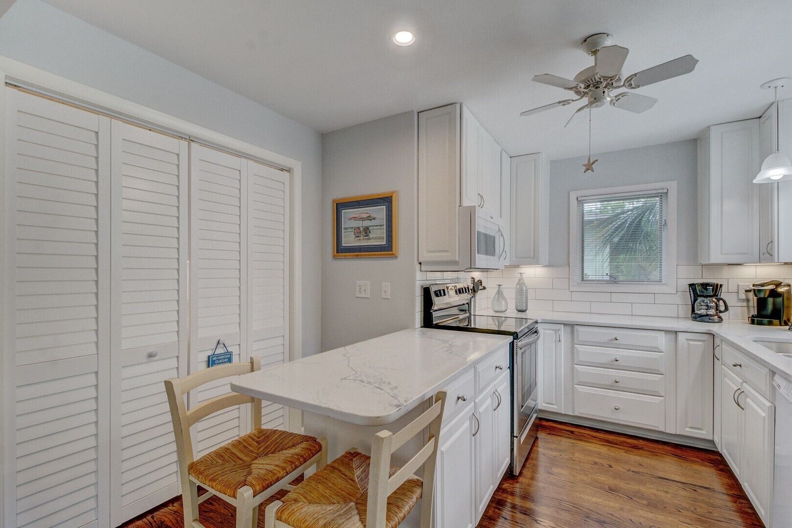 A kitchen with white cabinets, a marble countertop, and a ceiling fan.