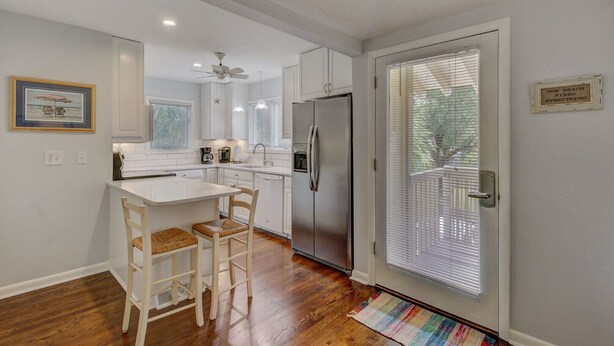 Una cocina moderna con armarios blancos, un refrigerador de acero inoxidable, un comedor con dos sillas y una alfombra colorida.