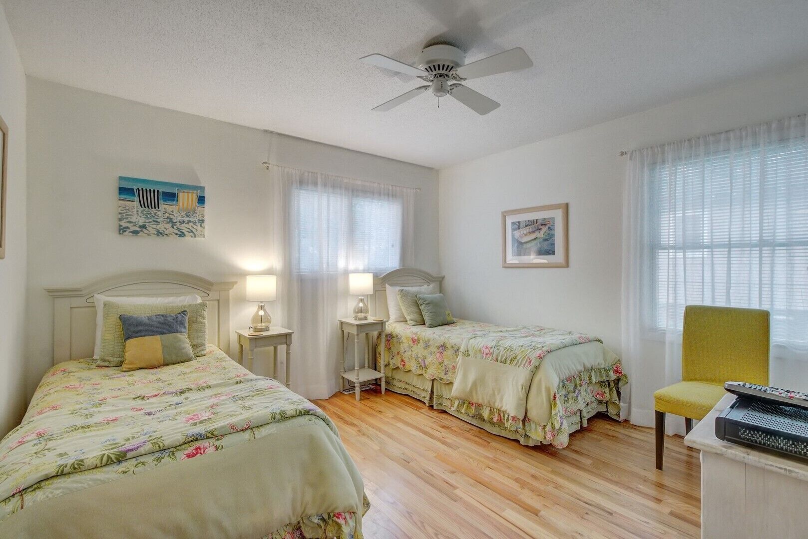A bedroom with two single beds, a ceiling fan, and a chair.