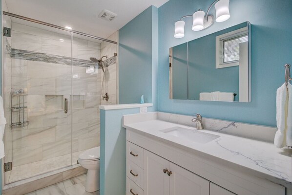 A modern bathroom with a glass-enclosed shower, a large mirror, and a white vanity with marble countertops.