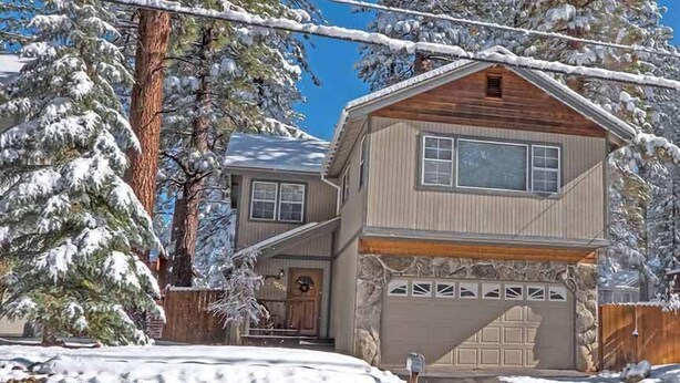Una casa de dos pisos con garaje, rodeada de árboles cubiertos de nieve.