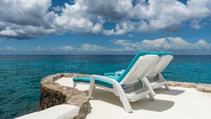 Two white lounge chairs with turquoise cushions on a white platform overlooking the ocean. - Delightful Oceanfront 3BR Condo South tower,the best Ocean views in the complex! (Cozumel)