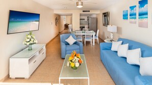 A living room with a blue sofa, a coffee table with a floral arrangement, and a dining area with a white table and chairs. - Delightful Oceanfront 3BR Condo South tower,the best Ocean views in the complex! (Cozumel)