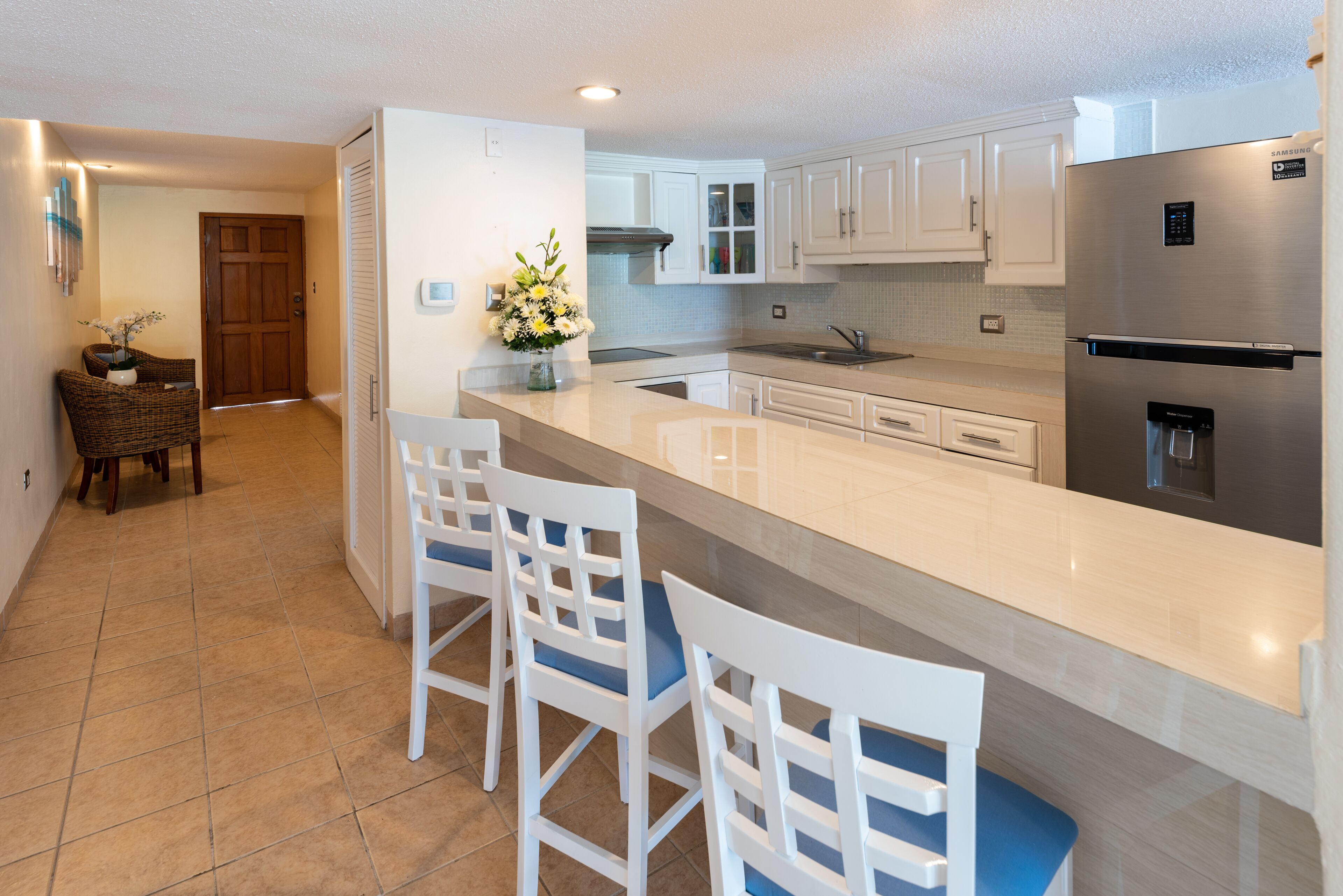 A modern kitchen with white cabinets, a stainless steel refrigerator, and a large island with bar stools.