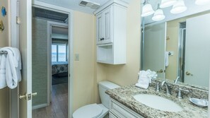 Baño con lavamanos doble, inodoro y ducha a ras de suelo. Se observa un espejo grande sobre el lavamanos y un perchero a la izquierda.