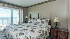 Una habitación de hotel con una cama, una mesita de noche, una lámpara y vistas a la playa.