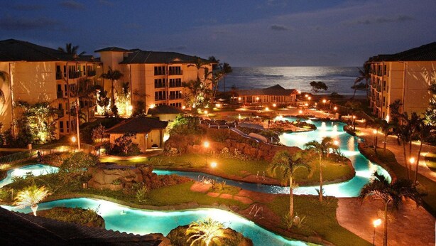 A resort with multiple swimming pools, a beach, and a view of the ocean at night.