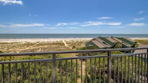 Ein Balkon mit Blick auf Strand und Meer, ein Gebäude mit grüner Dachbegrünung und ein klarer Himmel.