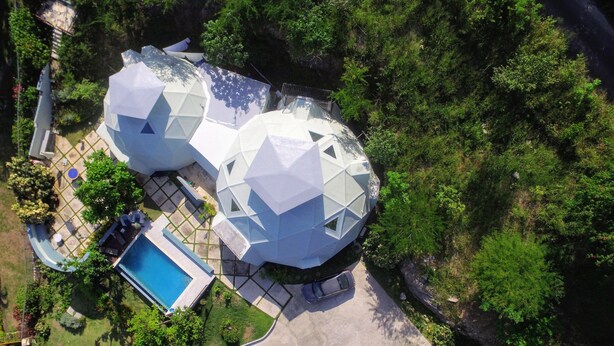 Vista aérea de una casa moderna con una estructura geodésica única, una piscina y un camino de acceso con un coche estacionado.