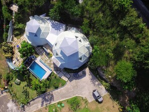 Vista aérea de una casa moderna con una estructura geodésica única, una piscina y un camino de acceso con un coche estacionado.