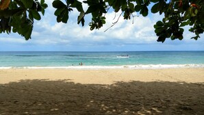 Una playa con cielos despejados, aguas tranquilas y un barco a lo lejos.
