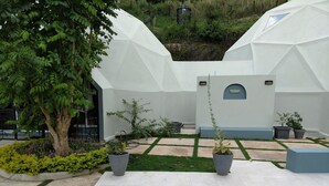 Un espacio exterior moderno con una terraza de madera, una piscina y dos estructuras blancas en forma de cúpula.