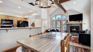 A spacious living area with a large wooden dining table, a fireplace, and a television mounted on the wall.