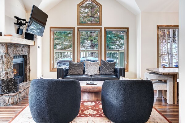 A cozy living room with a fireplace, a large window, a flat-screen TV, and a stone accent wall.