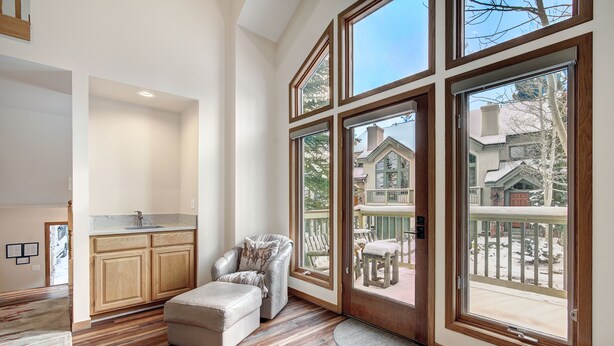 A spacious room with a large window, wooden flooring, a sofa, and a kitchen area.