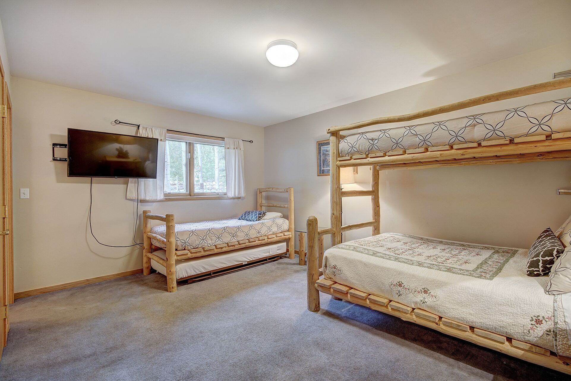 A bedroom with two wooden bunk beds, a television mounted on the wall, and a window with curtains.
