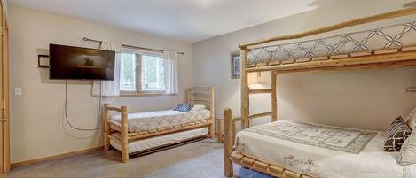 A bedroom with two wooden bunk beds, a television mounted on the wall, and a window with curtains.