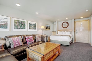 A hotel room with a bed, a leather sofa with patterned cushions, a wooden coffee table, and framed pictures on the wall. - Downtown Studio w/ Sunny Alpine Views- Sleeps 4! (Breckenridge)