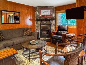 A cozy living room with a stone fireplace, leather sofa, and wooden chairs.