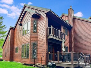 A two-story house with a balcony, a deck with outdoor furniture, and a chimney.