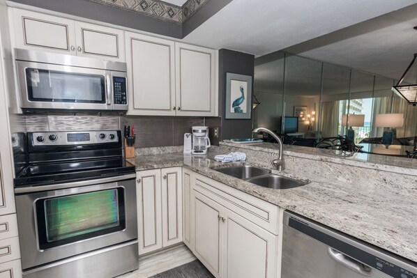A modern kitchen with stainless steel appliances, a granite countertop, and a large mirror reflecting the room. - E405 Lower floor, Great Gulf View, Gated Condo, 3 Pools (Panama City)