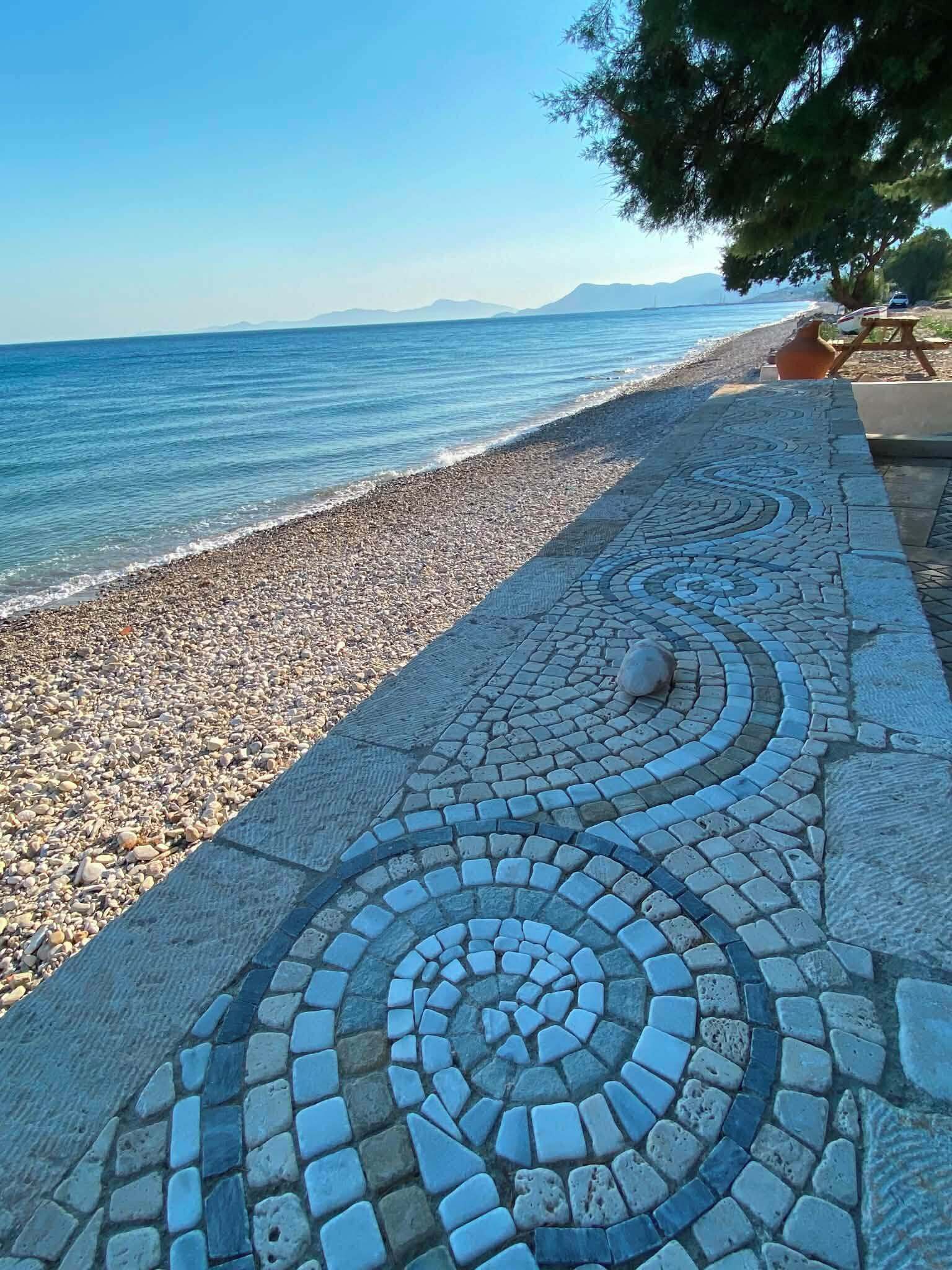 Una spiaggia di ciottoli con una passeggiata lastricata che conduce all'acqua.