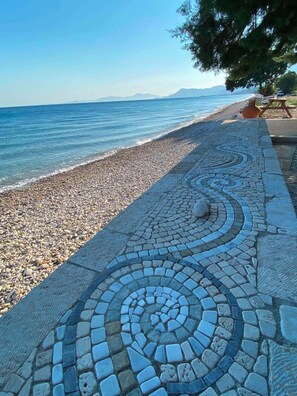 A pebble beach with a patterned walkway leading to the water.