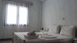Une chambre d’hôtel comprenant un lit, une table de chevet, une fenêtre avec des rideaux légers et un appareil de climatisation.
