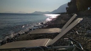 Une plage avec deux chaises longues vides, face à la mer, un rivage rocheux et des montagnes en arrière-plan.