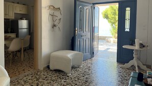 Une pièce avec un coin cuisine, un pouf blanc, une porte bleue et une vue sur la mer.