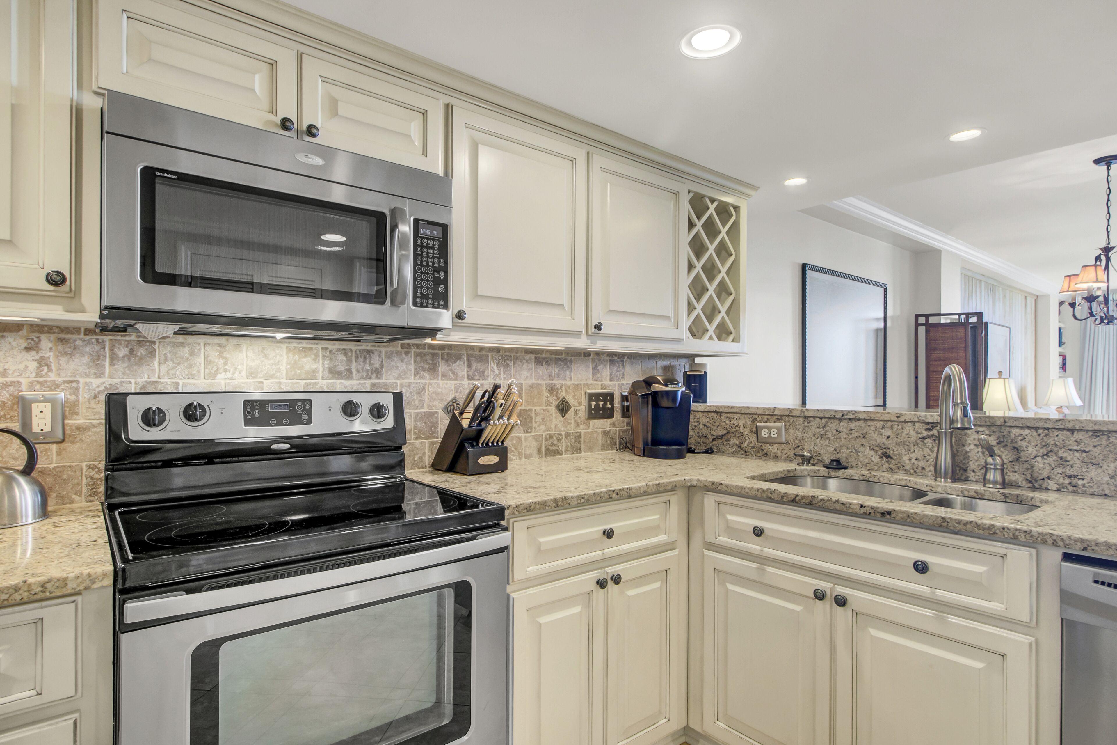 A modern kitchen with stainless steel appliances, white cabinetry, granite countertops, and a built-in dishwasher.