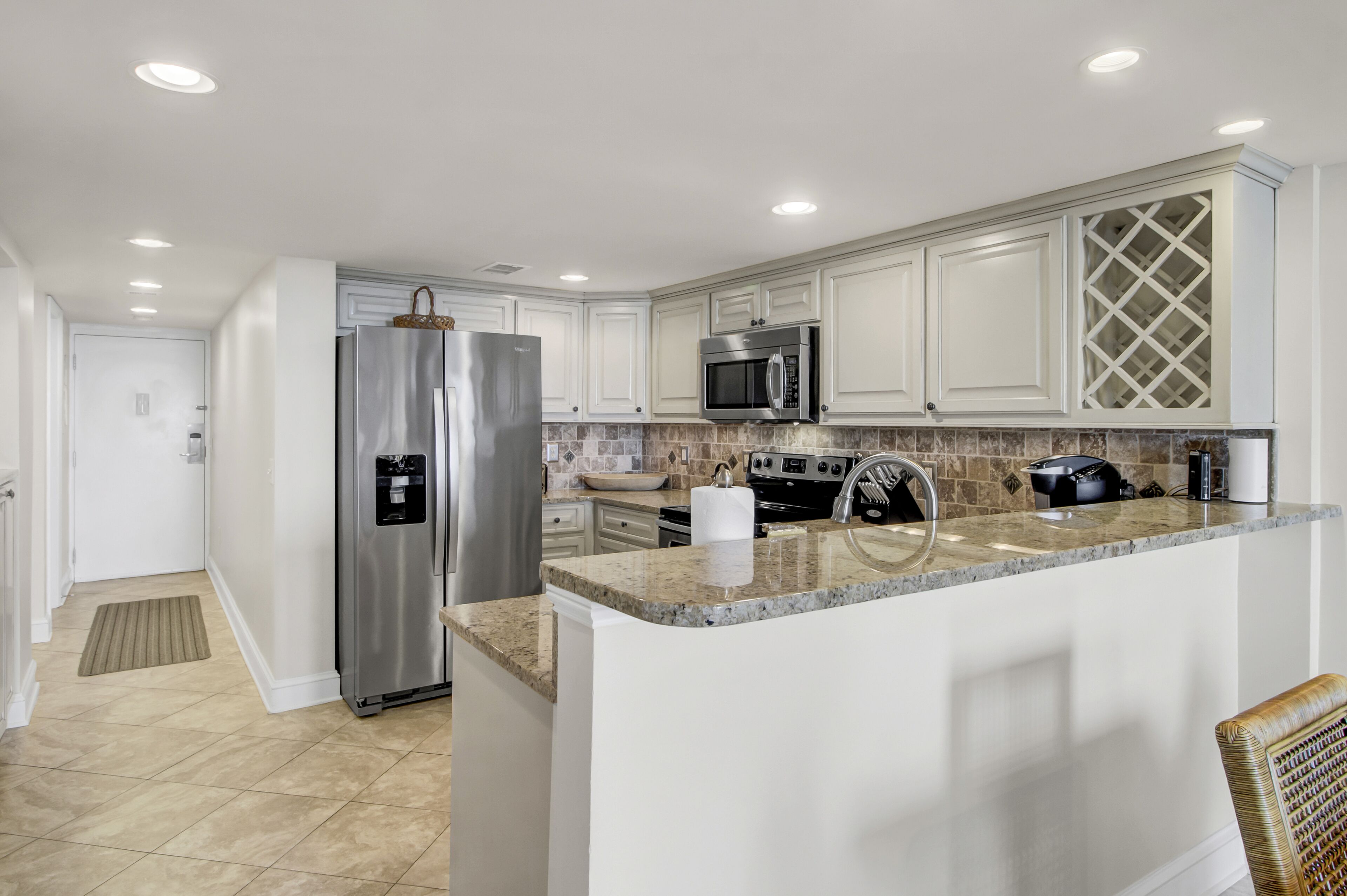 A modern kitchen with white cabinetry, stainless steel appliances, a granite countertop, and a built-in wine cooler.