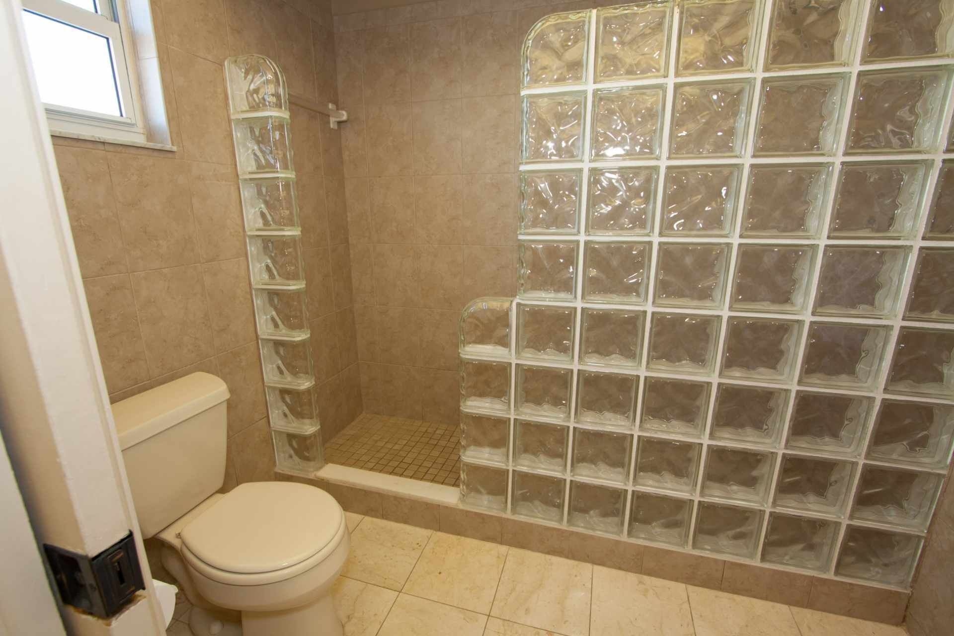 A bathroom with a toilet, a glass shower enclosure, and a tiled floor.