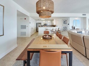 Una cocina moderna con armarios blancos, una isla central y un comedor con mesa de madera y sillas de cuero.