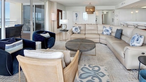 A spacious living area with a large sofa, a coffee table, and a wicker chair. There is a ceiling fan and a chandelier. - Coastal Castle. 4 Bedroom Gulf Front condo. (Navarre Beach)