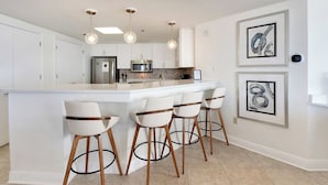 A modern kitchen with a central island, bar stools, pendant lights, and framed artwork on the wall. - Coastal Castle. 4 Bedroom Gulf Front condo. (Navarre Beach)