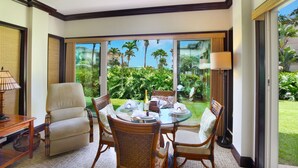 A room with a dining table set for four, surrounded by wicker chairs, a sofa, and a lamp. - Waipouli Beach Resort Exceptional Condo Pool View Condo (Kapaa)