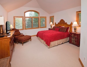 A bedroom with a large bed, a wooden desk, a chair, and a dresser. There are windows with blinds, a lamp on the dresser, and a television on the desk. - 4BR/4BA Private Rustic Home in Arrowhead - Quick Shuttle to the Lift! by RedAwning (Edwards)